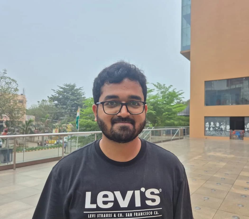 Chaitanya Raj standing on an open terrace, trees and a glass railing to one side and a low orange building behind him.